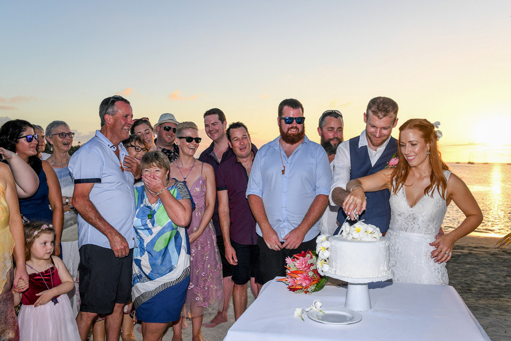 Guests watch as the couple cut the brilliant white tropical frangipani cake at sunset