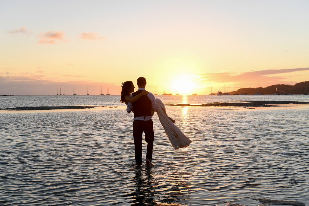 A silhouette of the groom carrying his bride into the sea at sunset