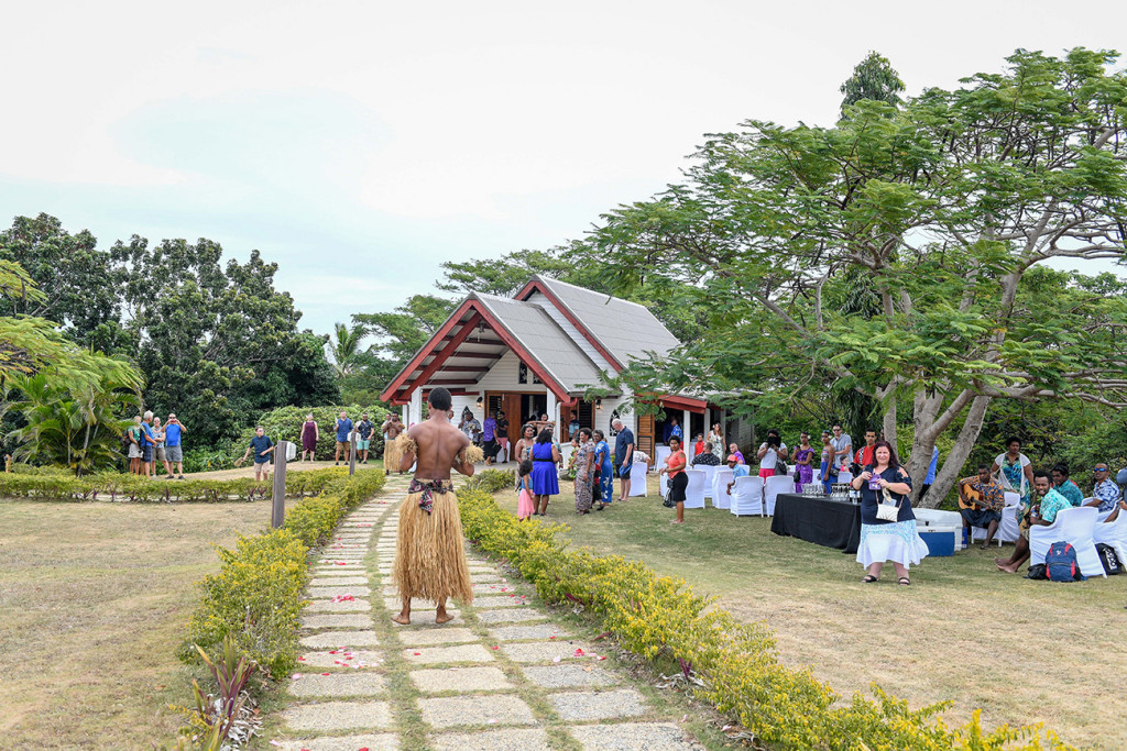 Fiji groomsman dressed in traditional Fiji masi walks down the aisle as guests watch
