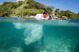 Bride and groom kiss just above water while their bodies are underwater