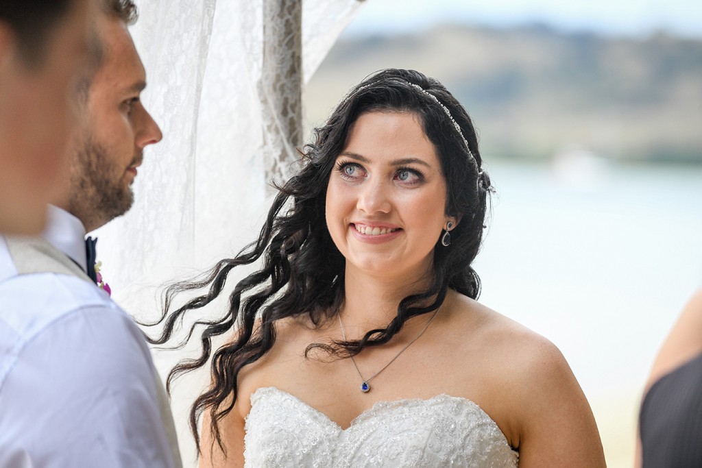The bride has a big grin as she watches her husband while at the altar