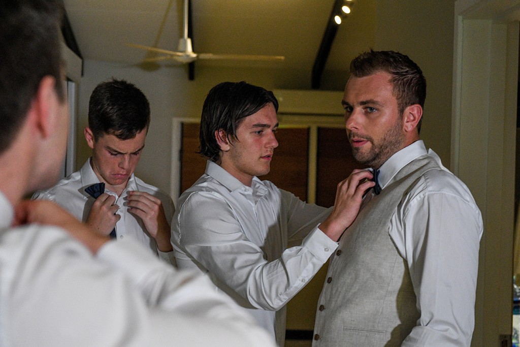 A groomsman helps the groom tie his tie