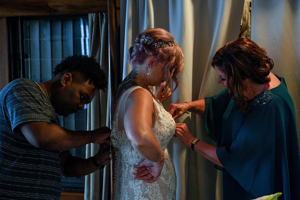 The bride's mother and makeup artist make adjustments to the bride's dress