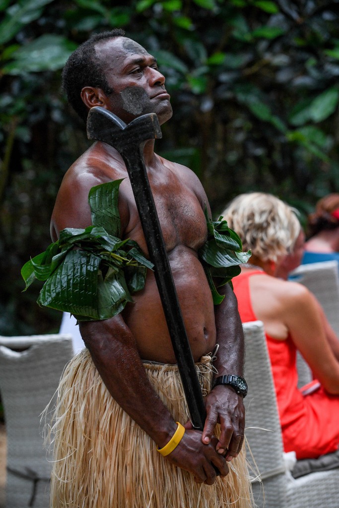 A traditional Fiji warrior in banana leaves and sisal skirt watches on