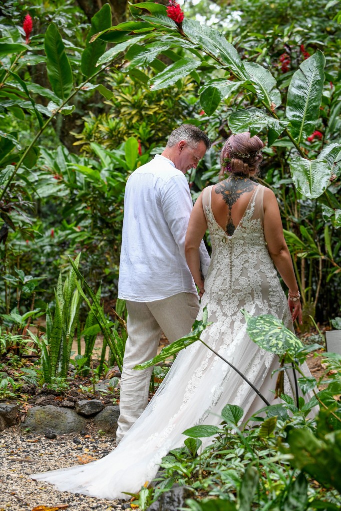The newly weds hold hands as they stroll into the rain forest