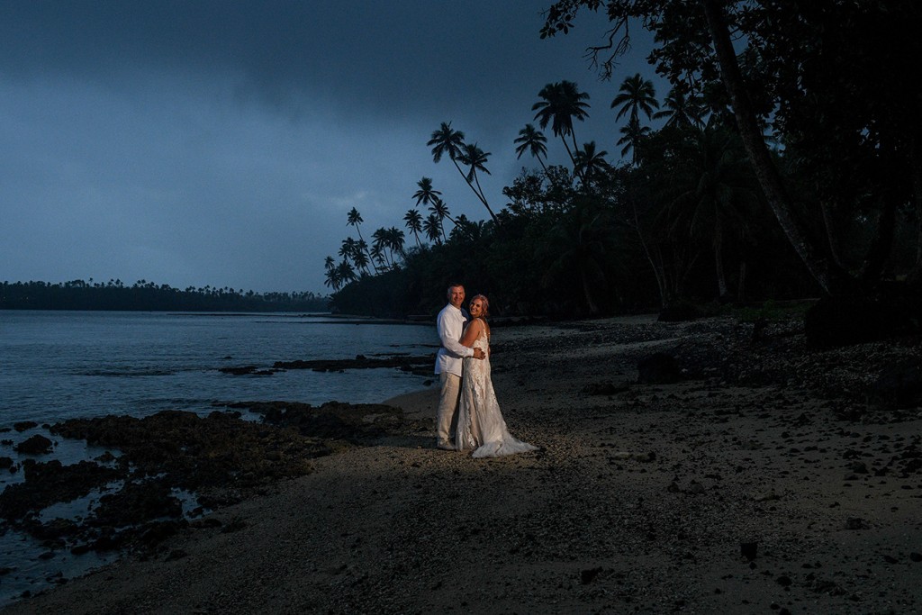 The newly weds pose against silhouetted palm trees after sunset