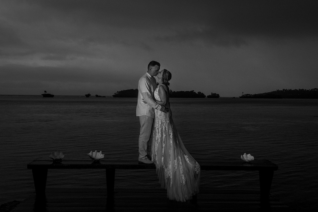 A monochrome photo of the newly weds share a passionate kiss on the dark Fiji beach