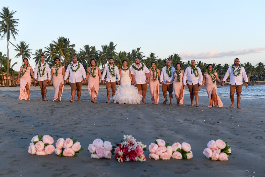 The bridal party poses with their flowers in the foreground on the black sand beach of Sheraton Fiji