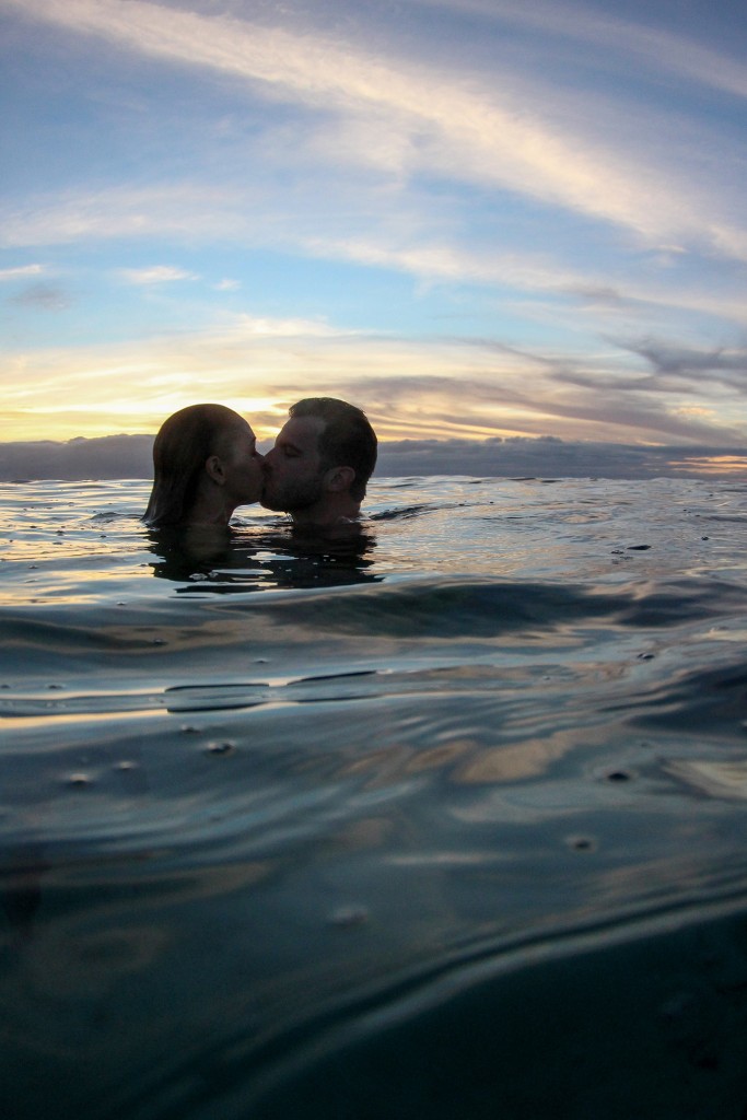 The couple kisses passionately above water at sunset