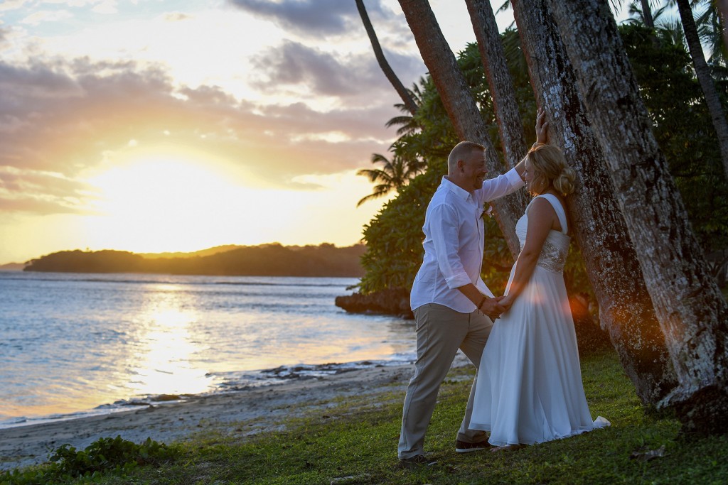 The newly weds cosy up against a palm tree during a fiery Fiji sunset