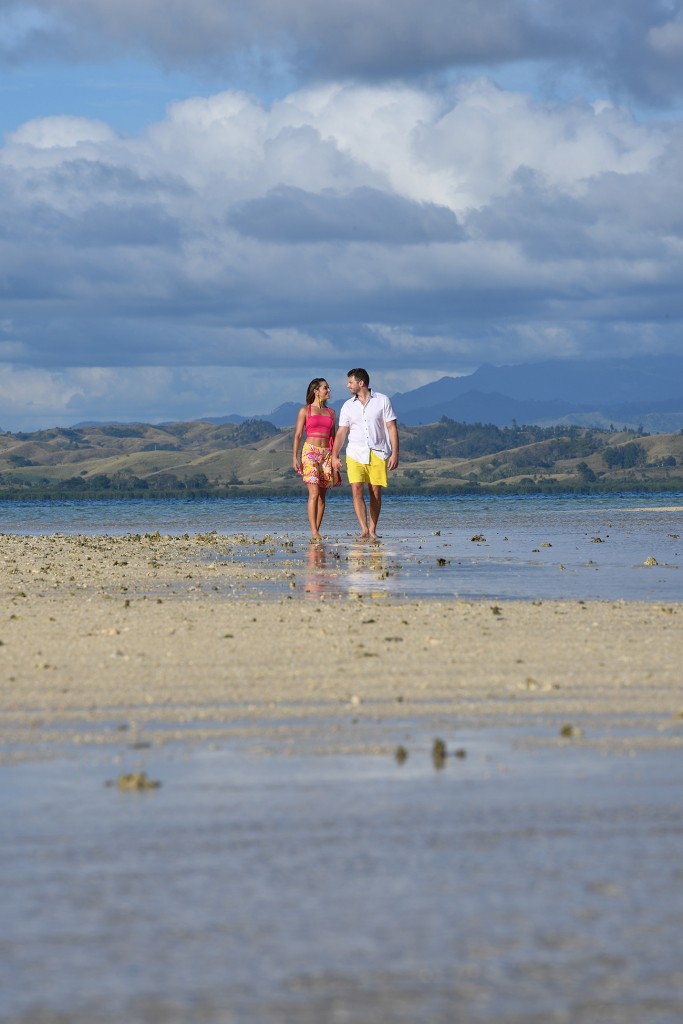 The couple strolls on the beach against grey Fiji skies