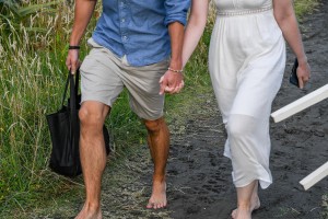 The married couple walks hand in hand on the black sand beach at Karekare