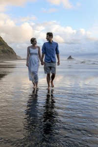 The newly weds hold hands as they walk in shallow Karekare beach
