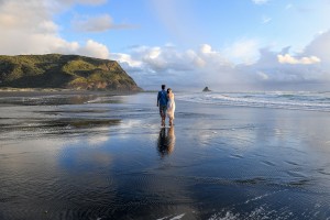 The couple holds hands standing in breathtaking nature at Karekare beach