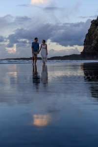 The newly weds stroll on the shallow waters of the black sand beach at Karekare