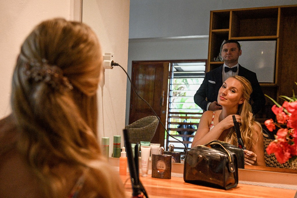 A reflection of the groom checking out her bride as she curls her hair in the mirror