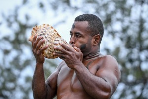 A traditional Fiji warrior blows a shell horn to announce the arrival of the bride