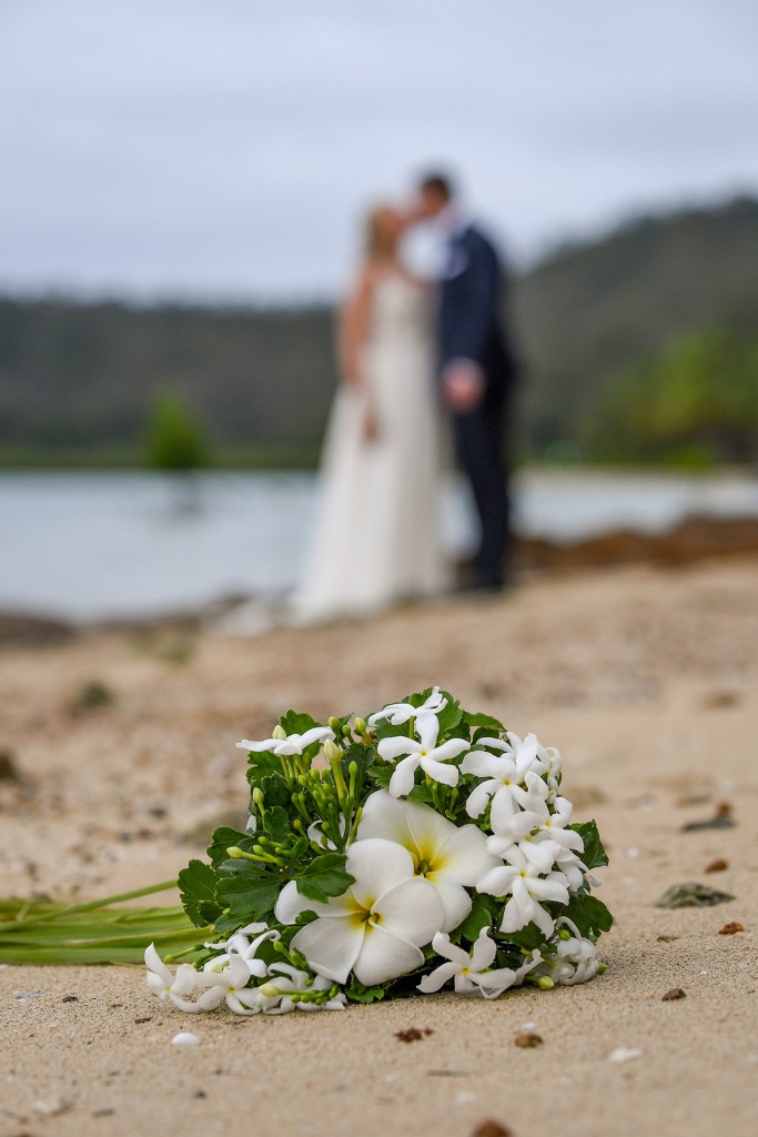The newlyweds kiss in the background of white frangipanis