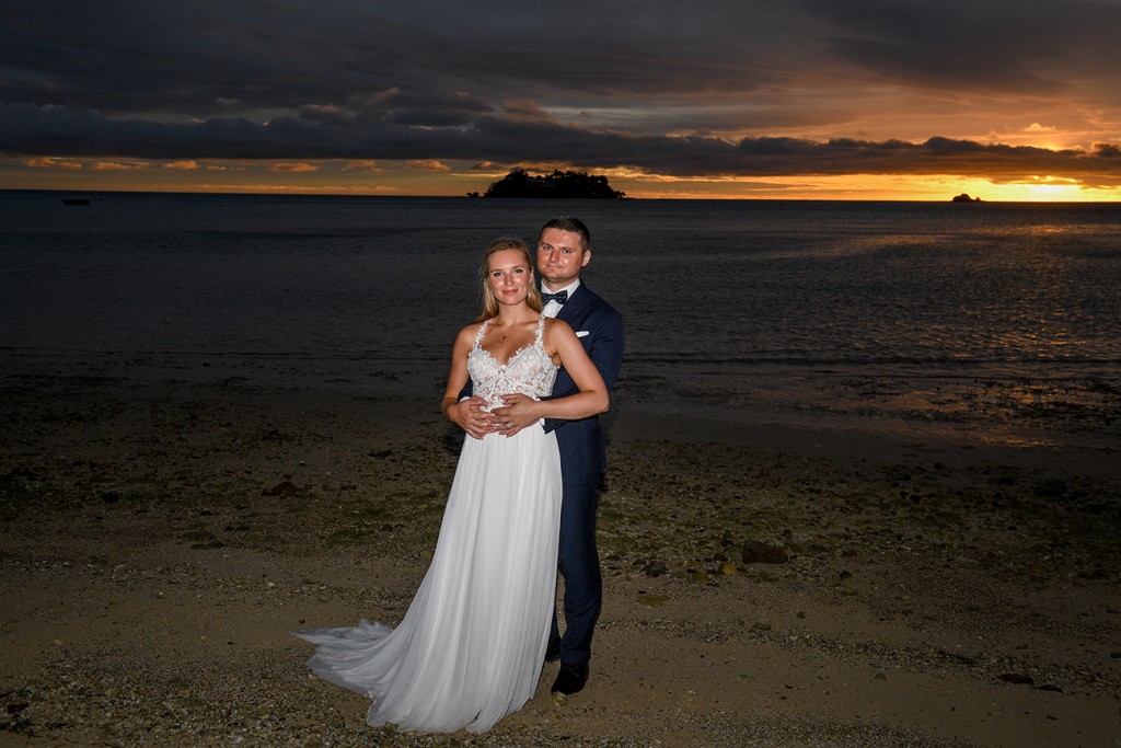 The newly weds pose with a fiery sun setting behind them