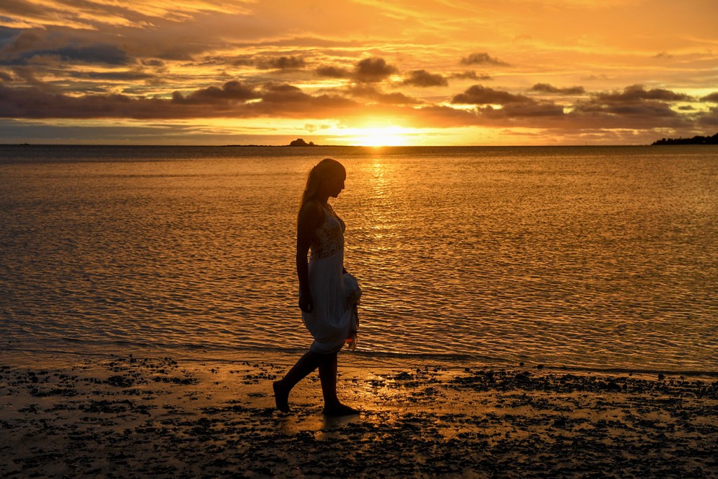 A silhouette of the bride strolling the shores of the Pacific at sunset