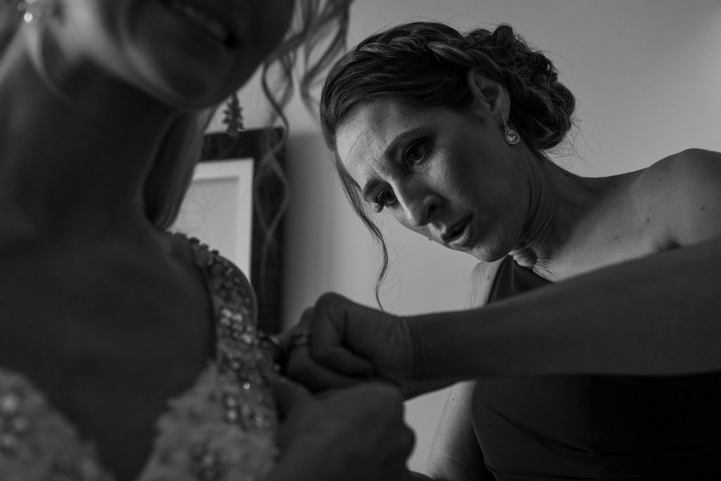 The bridesmaid helps fasten bride's dress which he helps fasten
