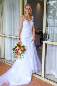 The stunning bride poses in the doorway in a brilliant white gown and fresh Fiji flower bouquet