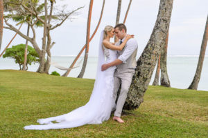 The newly weds share an intimate moment cuddling against a leaning palm tree