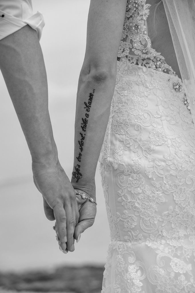 A monochrome image of the newly weds holding hands with bride's Life's too short tatoo