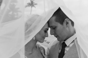 A monochrome portrait of the newly weds posing under the bride's veil