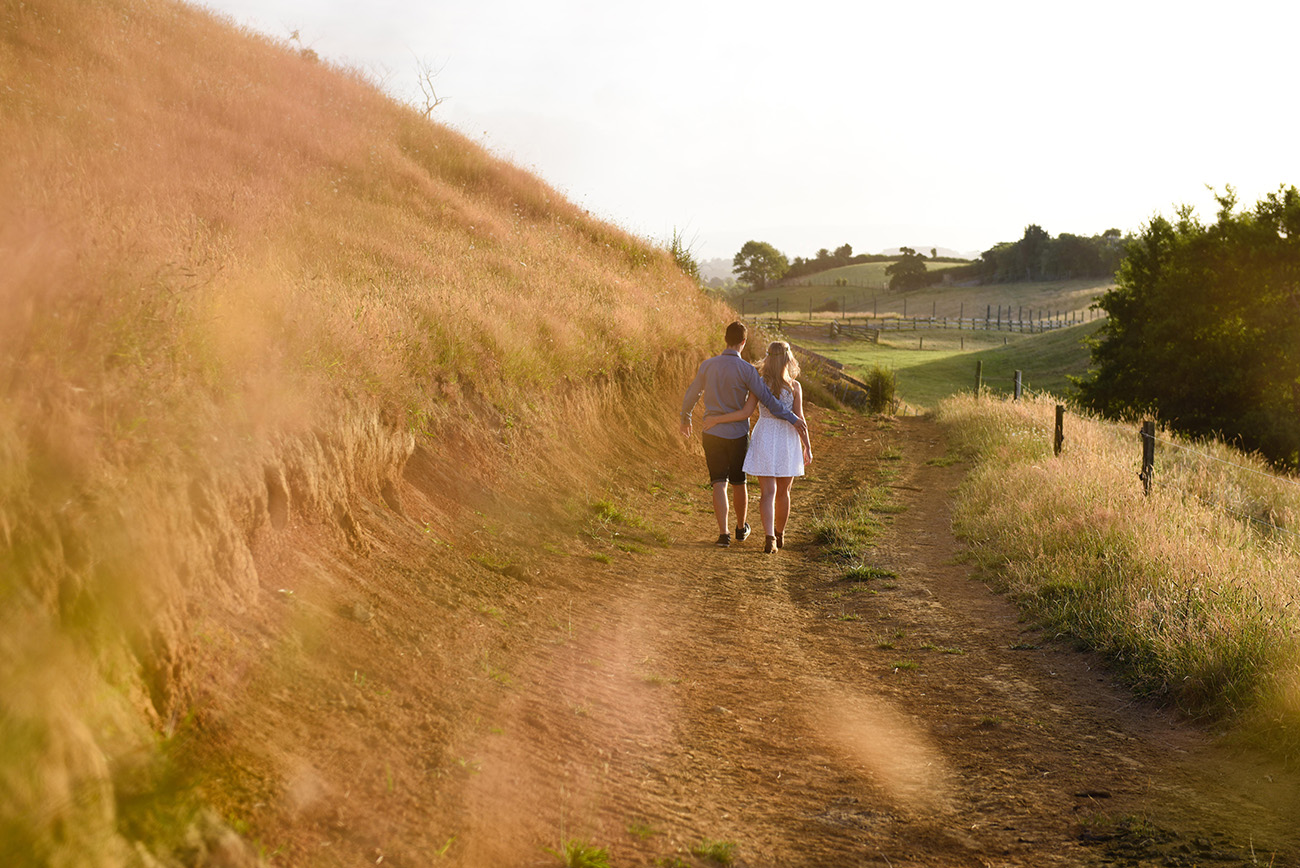 The engaged couple stroll down a dirt road Summer Engagement photo shoot in the country Pukekokhe Auckland Photographer Anais Chaine