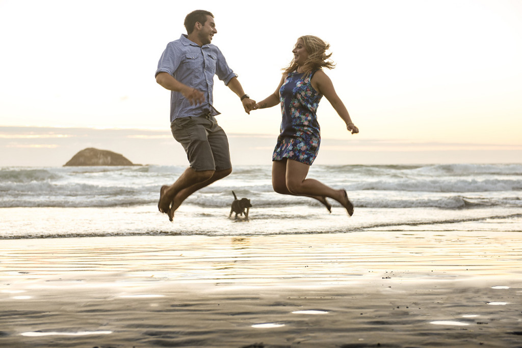 young engaged couple jumping by the beach
