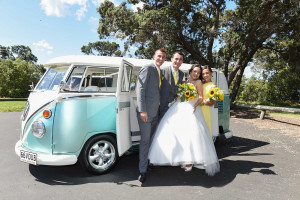 in front of the turquoise vintage van the bride and groom with their brother and sister smiling and posing
