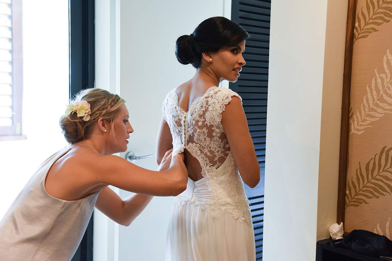 One of the bridesmaids adjusting the wedding dress' lace on the bride's back
