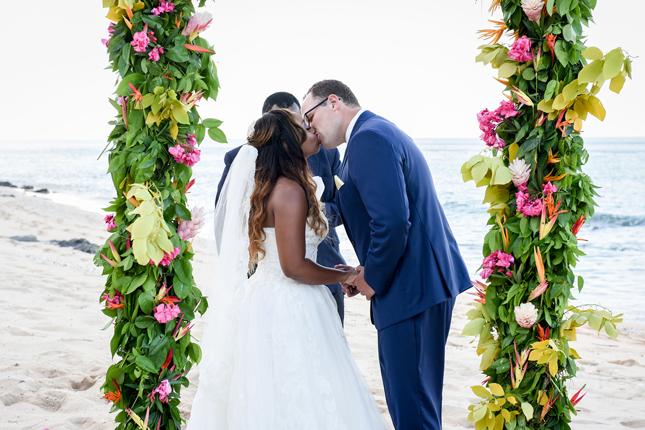 The bride and groom are doing the first kiss by the floral arch At Paradise Cove Island resort in the Yasawas, Fiji