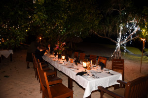 The table is set up in the beach with the white sand, lanterns and ferry lights at Paradise Cove island resort in the Yasawas in Fiji photographed by Anais Photography