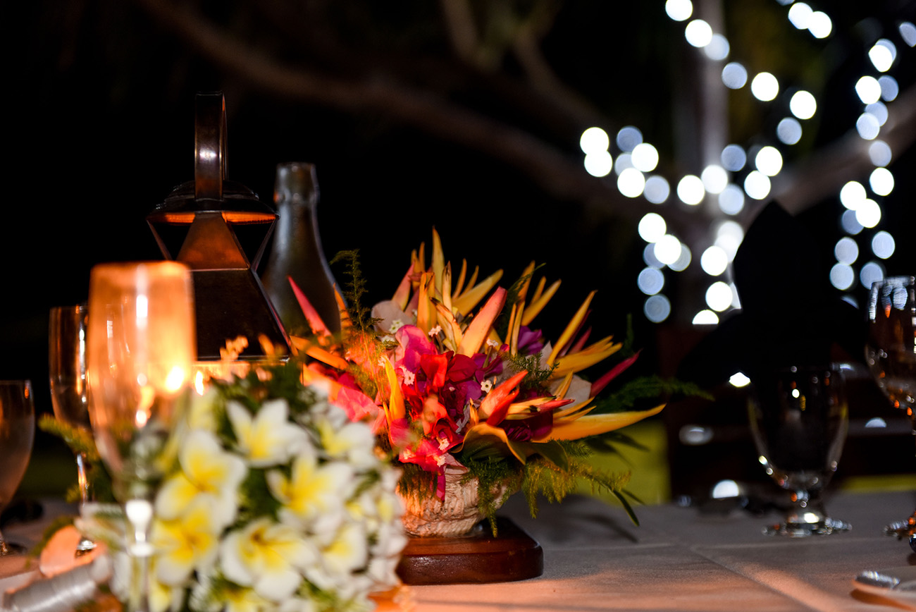 A tropical bunch of flowers is the central piece f the wedding table with ferry lights in the background at Paradise Cove island resort in the Yasawas in Fiji photographed by Anais Photography