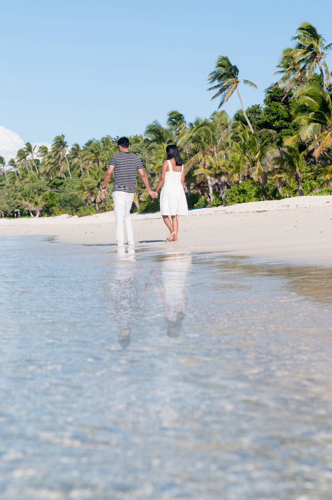 Couple holding hands from the back walking along the beach at Mana Island resort, Fiji by Anais Photography