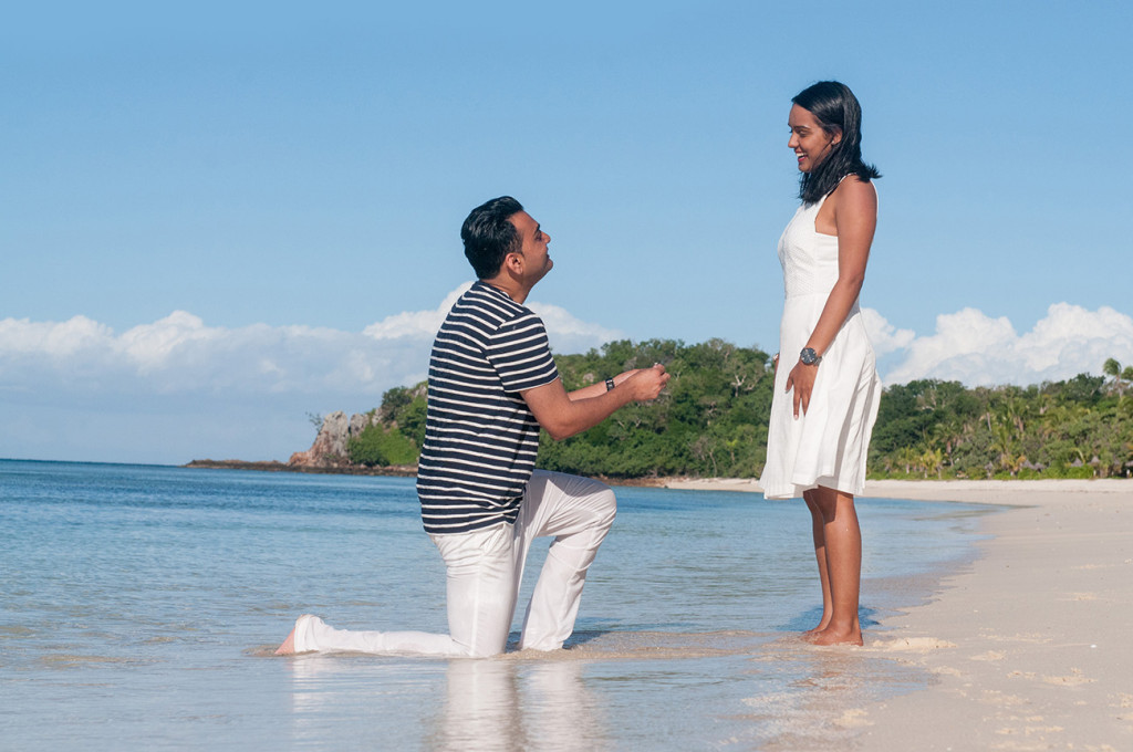 The man is kneeling down in the sea by the beach proposing to his girfriend to become his wife at Mana Island resort, Fiji by Anais Photography