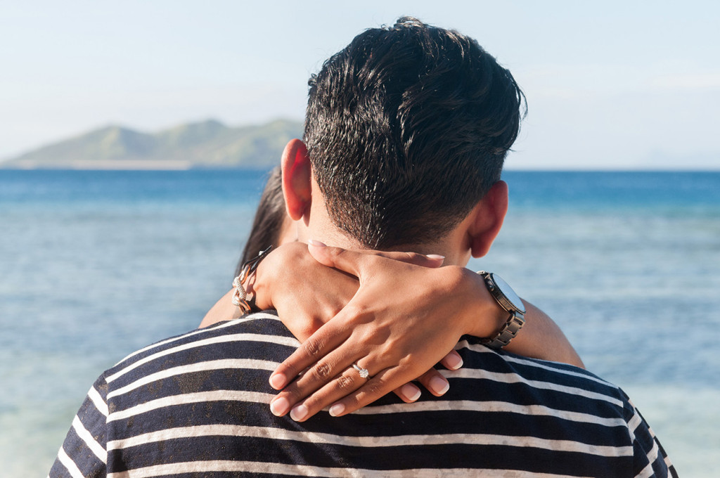 The fiancee has her arms around her fiance's neck with her new engagement ring at Mana Island resort, Fiji by Anais Photography