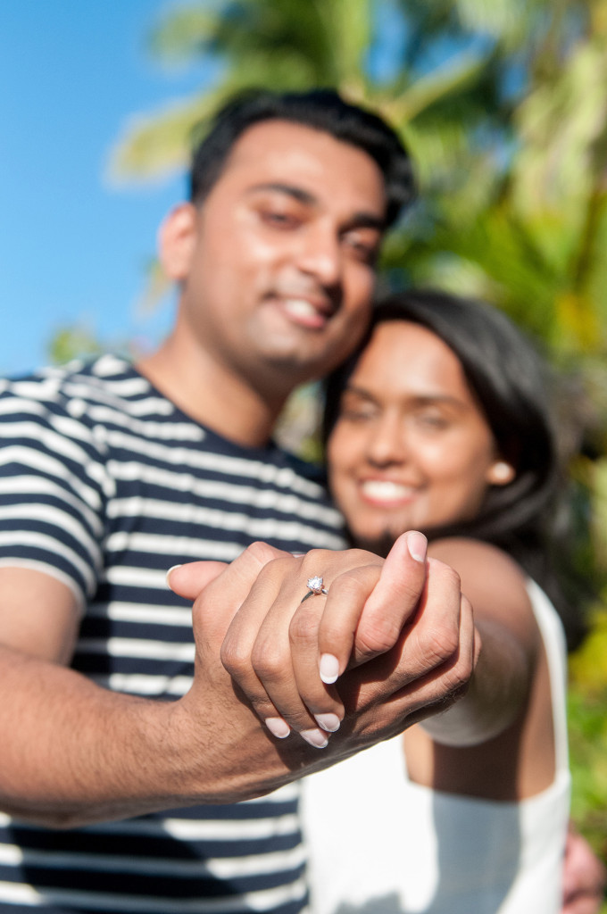 Diamond engagement ring with couple holding hands and their faces blurred in the background at Mana Island resort, Fiji by Anais Photography