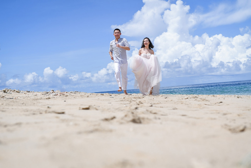 Bride and groom are running along the beach and its white sand at Paradise Cove island resort, Fiji
