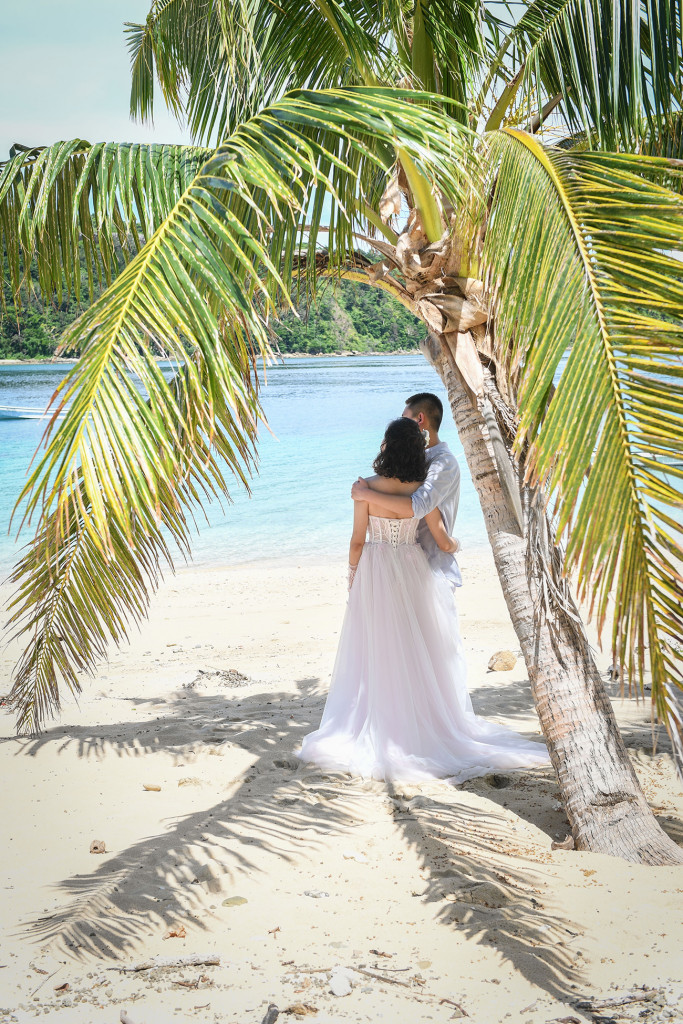 Bride and groom in the shade of a palm tree Paradise Cove island resort, Fiji