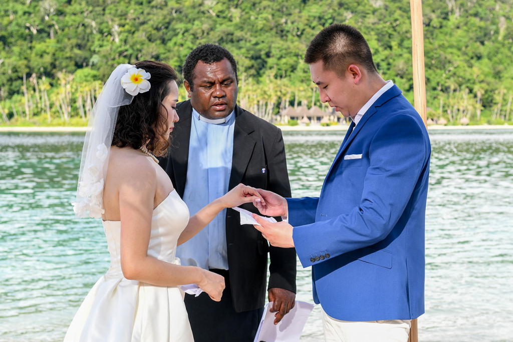 The groom is putting the ring on his wife's finger at Paradise cove island resort, Yasawas, Fiji