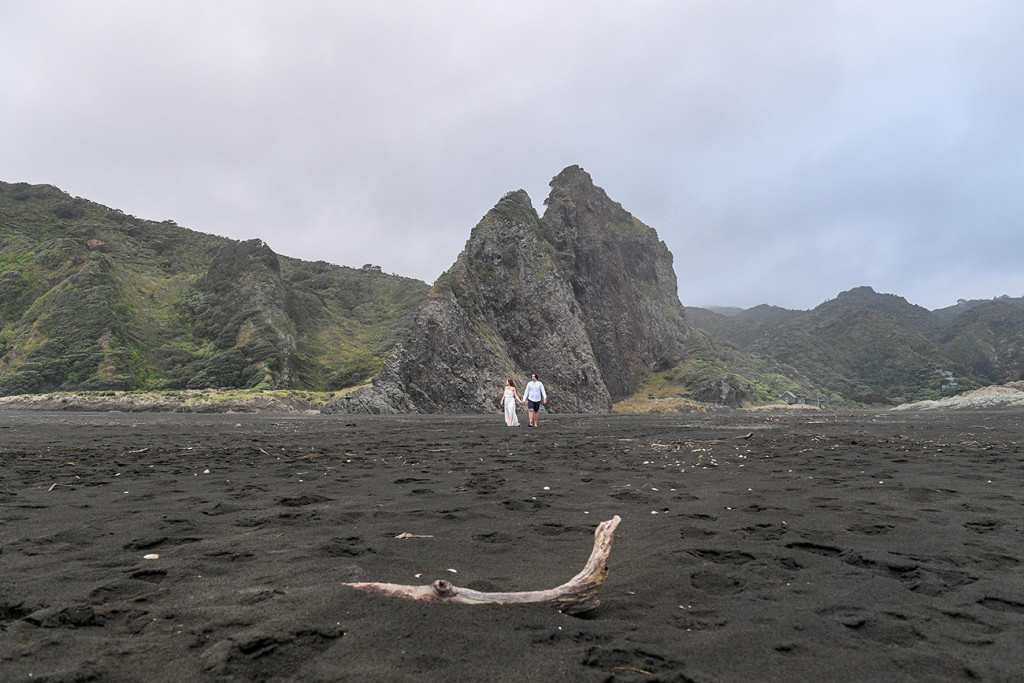 Landscape shot of Newly eloped couple on black sand beaches of Karekare NZ