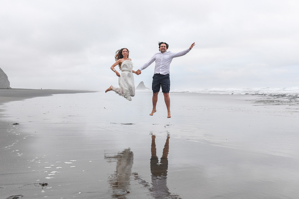 Newly eloped couple jump in black sand Karekare Beach Auckland NZ