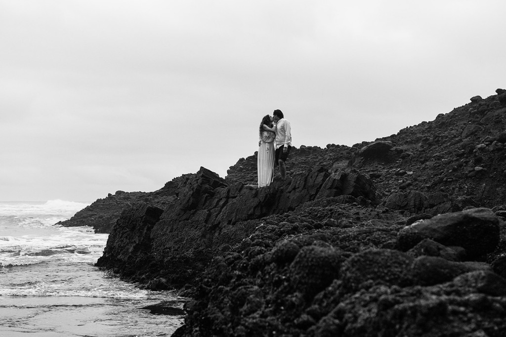 Black and white photo of newly eloped couple kissing on Karekare Beach NZ