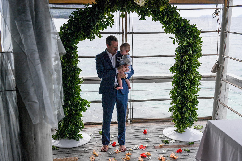 Groom holds son in his arms at the altar Vomo Island Resort