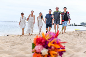 Married couple and wedding guests walk on beach with orange and pink bouquet soft in the foreground