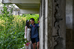 Married asian couple kiss against abandoned building and overgrown background