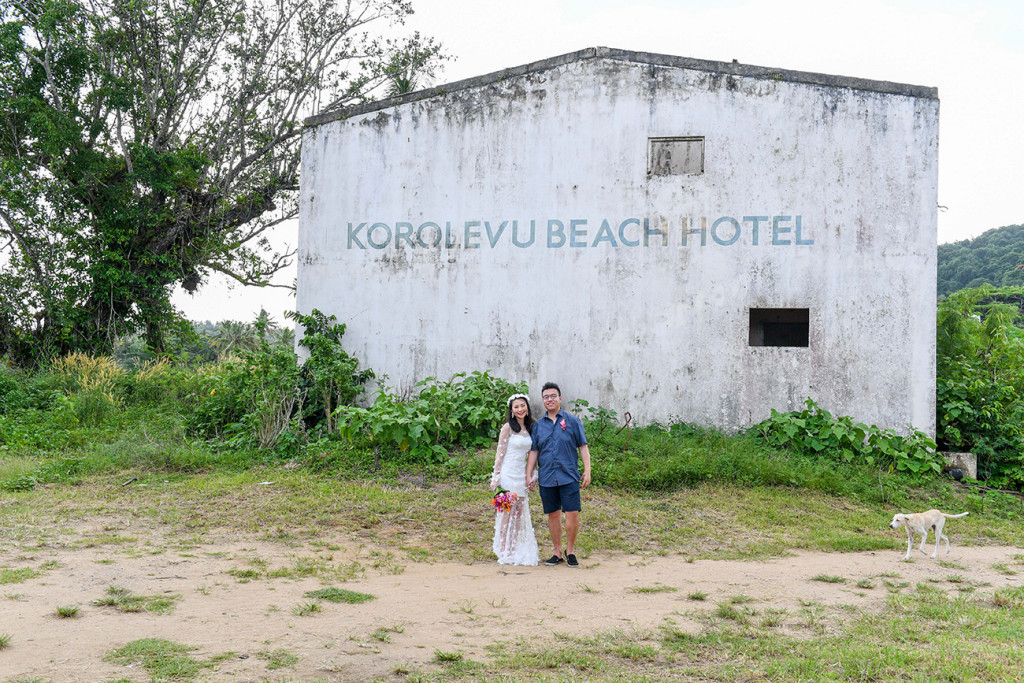 Wide shot of newly married couple standing against abandoned building in Warwick Fiji
